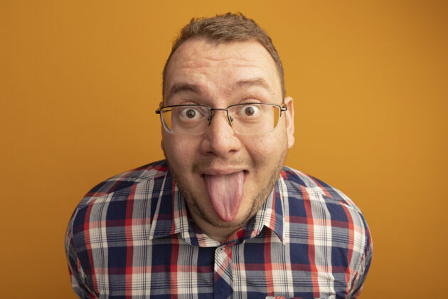眼镜戴着眼镜和格子衬衫的滑稽男人站在橙色的墙上伸出舌头站搞笑男人