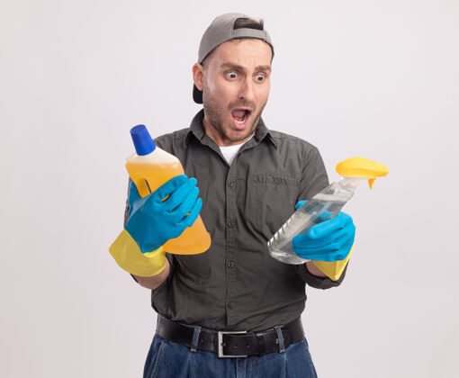 举行年轻的保洁员穿着休闲服 戴着橡胶手套 手里拿着喷雾瓶和清洁用品 站在白色的墙壁上惊讶不已手套清洁穿