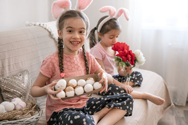 装饰有兔子耳朵的小姐妹们摆出复活节彩蛋和鲜花作为装饰孩子托盘女孩