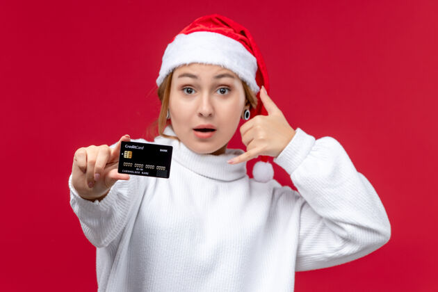 圣诞节正面图：年轻女性在红色背景下与银行卡合影红色人帽子