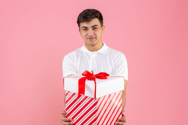 正面正面图：年轻男性 带着大大的圣诞礼物 在粉色背景上微笑着视图肖像年轻男性