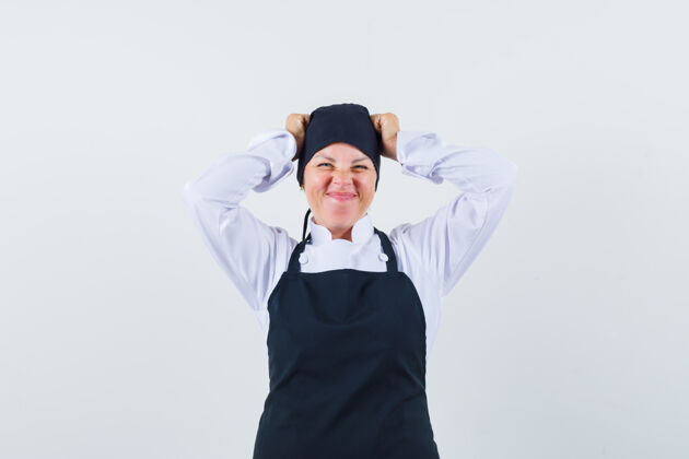 魅力穿着黑色厨师制服的金发女人 手举在头上 做鬼脸 看起来很漂亮烹饪可爱鬼脸