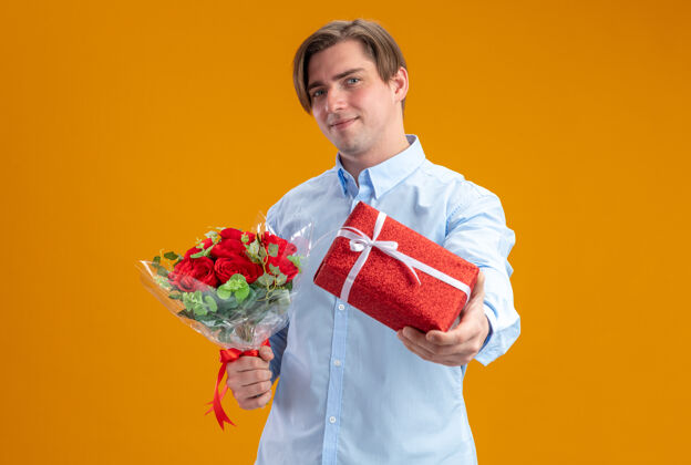 情人节身穿蓝衣的男子手持一束红玫瑰 站在橙色的墙上 看着相机微笑着自信的情人节概念日子玫瑰看