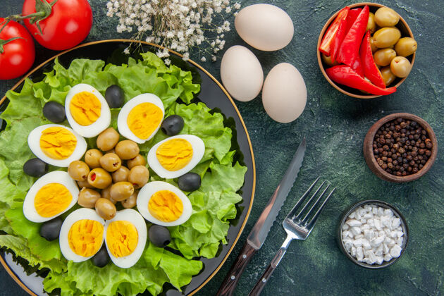 背景俯视图煮熟的切片鸡蛋和绿色沙拉和橄榄在黑暗的背景橄榄蔬菜饮食