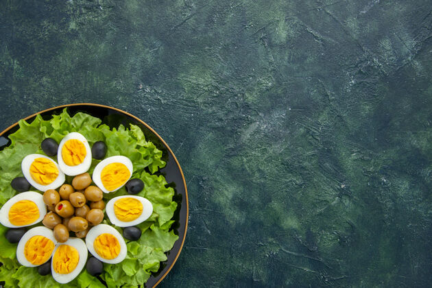 盘子顶视图煮熟的切片鸡蛋和橄榄和绿色沙拉在黑暗的背景晚餐绿色沙拉