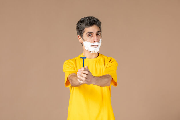 身体护理正面图：年轻的男性 脸上有泡沫 手上拿着剃刀 背景是粉色的人视图年轻男性