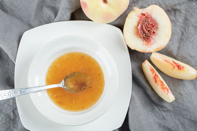 吃在灰色桌布上放着果酱和桃子的白色盘子可食用好吃好吃