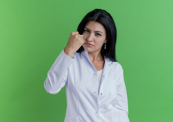 女性自信的年轻女医生穿着医用长袍做着坚强的姿态隔离在绿色的墙上和复印空间手势强壮表情