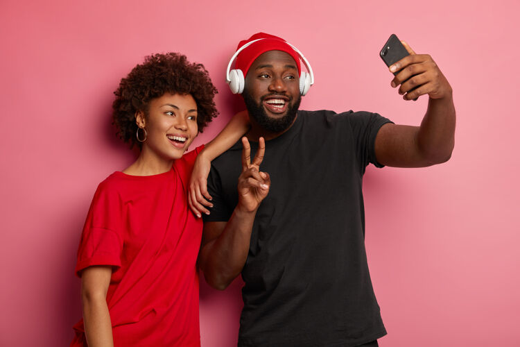 年轻年轻的美国黑人男女在现代小玩意上自拍 做出和平的姿态 对着镜头开心地微笑朋友衣服男性