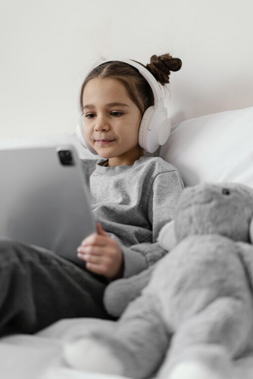 房子小女孩在床上用耳机用平板电脑科技室内设备