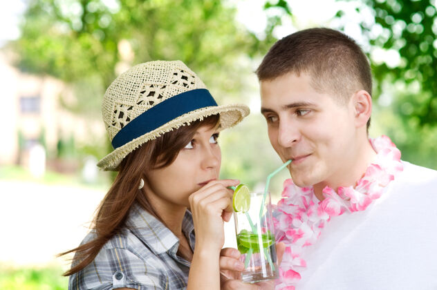面对面可爱的夫妇喝着莫吉托椰子酱吸管做一张脸玻璃杯