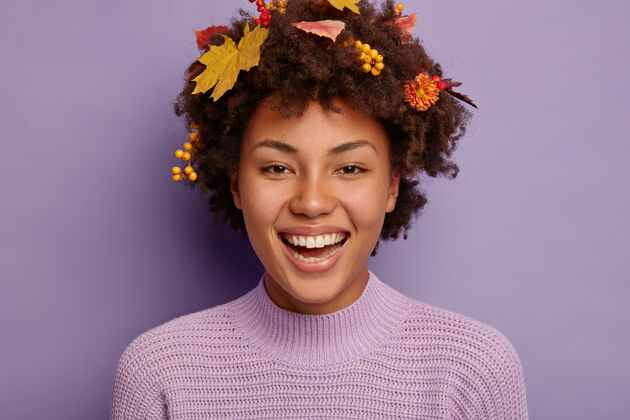 表情快乐温柔的非洲发型女人的画像笑容灿烂 露出洁白的牙齿 享受美好时光 头上有秋叶树叶高兴秋天