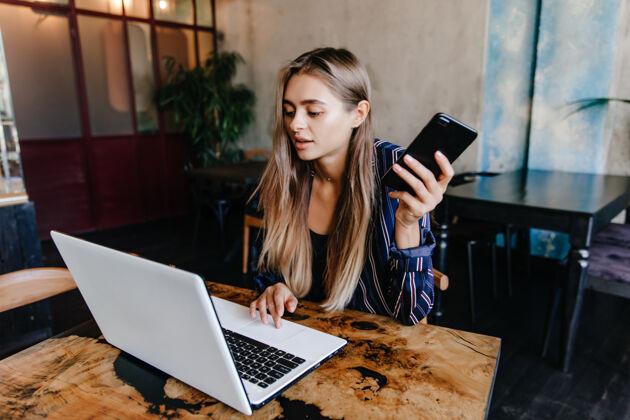 咖啡馆神奇的白人女孩手拿智能手机和笔记本电脑迷人的女自由职业者坐在咖啡馆成人笔记本电脑女孩