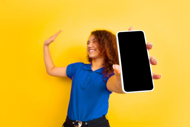 金融显示手机屏幕黄色墙上的白人少女肖像穿着衬衫的漂亮女性卷发模特人类情感的概念 面部表情 销售 广告 教育版权空间女性手表演