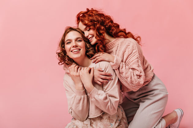 女孩两个卷曲的女孩拥抱在粉红色的背景上幸福的朋友在一起玩得开心粉色女性姜黄色