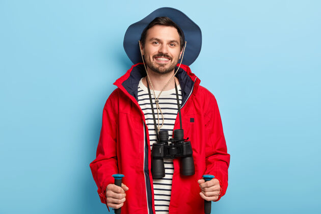自然积极的男性旅行者在森林里行走 积极的度假 积极的微笑 穿着时髦的帽子和红色夹克 脖子上戴着望远镜人背包度假