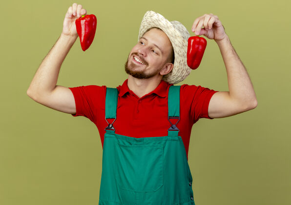 胡椒微笑着的年轻英俊的斯拉夫园丁 穿着制服 戴着帽子 看着辣椒橄榄微笑制服