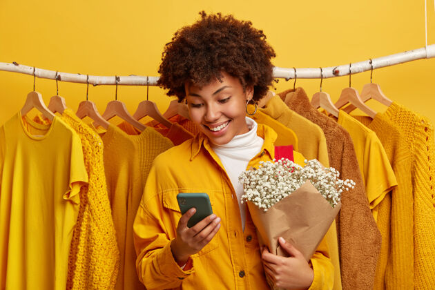 衣架积极卷曲的少数民族女性专注于智能手机设备手持花束人类短信零售