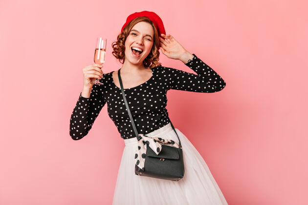 舞蹈快乐的法国女孩拿着酒杯摄影棚拍摄的微笑卷曲的贝雷帽女子孤立的粉红色背景欢乐香槟微笑