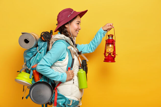高兴笑容可掬的亚洲女人拿着小油灯 去黑暗中探险 拎着随身物品的背包徒步旅行瓶子女人