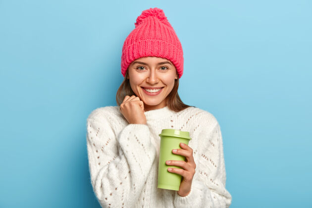 服装时髦的女学生拿着外卖咖啡 穿着暖和时髦的衣服 课后休息 在蓝色的墙上摆姿势舒适套头衫休闲