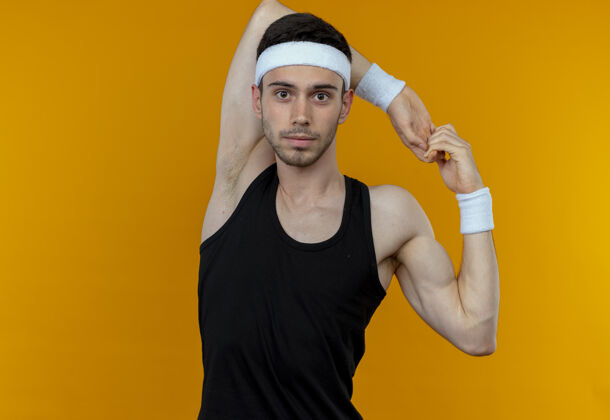 年轻戴着头巾的年轻运动型男子把手伸到橘子上站手头带