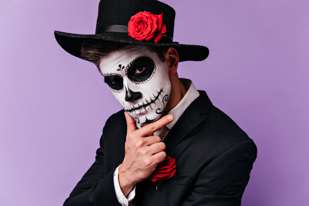 拉丁带着墨西哥传统妆容的沉思男人看着镜头万圣节派对前穿着僵尸服装的家伙摆姿势的摄影棚照片玫瑰嘉年华幽灵