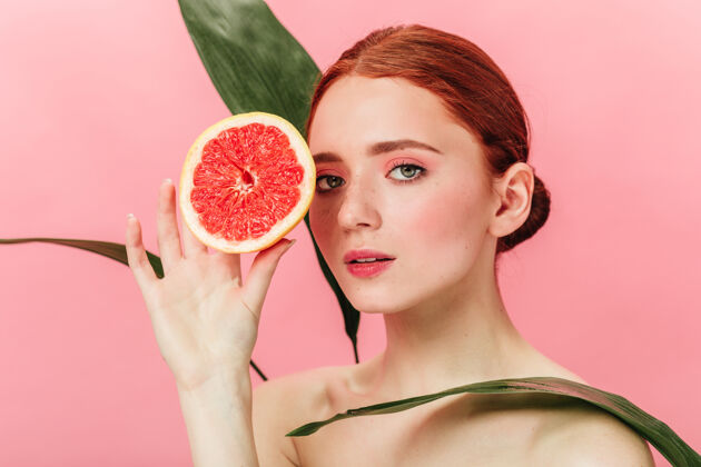裸体灵感女孩摆出绿叶和柑橘的姿势工作室拍摄的姜汁女人站在粉红色背景上的葡萄柚葡萄柚年轻人女孩