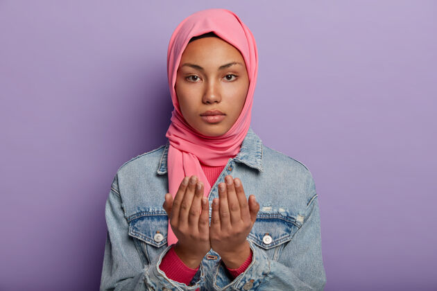 牛仔布平静迷人的阿拉伯女人保持手掌祈祷的姿势 戴着粉色头巾和牛仔夹克严肃东方姿势