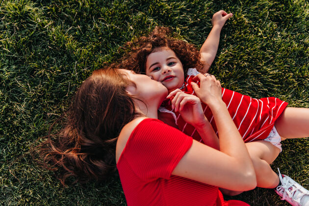 情绪夏日里幸福的家庭在一起冷冷清清的俯瞰图户外拍摄的黑发女子躺在草地上亲吻她的小女儿公园快乐游戏