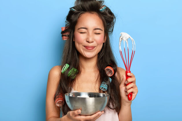 准备快乐美丽的韩国女士的肖像拿着搅拌器和碗 为饼干蛋糕做甜奶油 戴着卷发器黑发烹饪烹饪