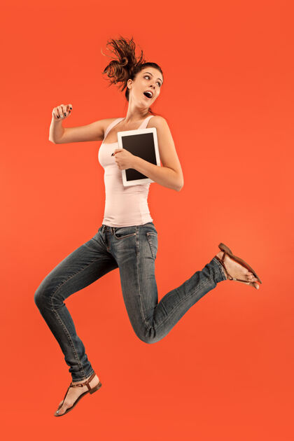 无线年轻女子跳过蓝色工作室使用笔记本电脑或平板电脑小玩意 而跳跃成功博客成人