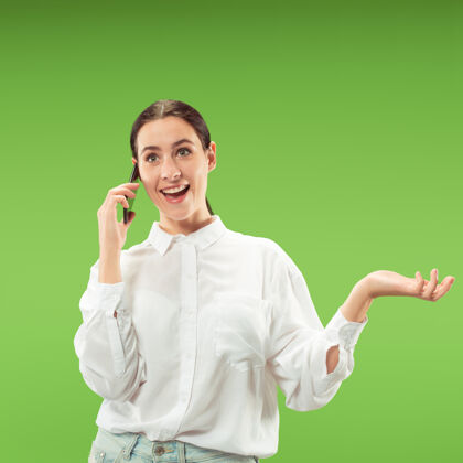 手机年轻漂亮的女人在绿色的墙上用手机人的面部情感概念成人科技使用