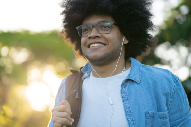 衣服年轻的非洲裔拉丁男子一边在街上散步一边用耳机听音乐的画像快乐休闲微笑