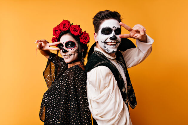 死亡日站在黄色墙壁上的大笑僵尸在万圣节派对上 一对可爱的墨西哥化妆情侣让人心寒幽灵墨西哥帽子