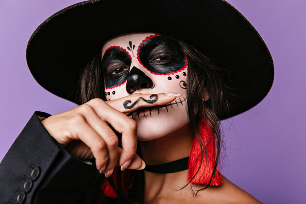 化妆戴宽边帽的聪明女孩的快照 画的是留着胡子的墨西哥男人黑发女士在淡紫色的墙上摆姿势万圣节头发黑发