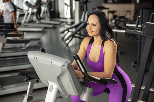 杠铃即将到来年轻肌肉发达的高加索妇女在健身房练习有氧运动运动女模特做速度练习 训练她的下半身 上半身健康 健康的生活方式 健美力量物理身体