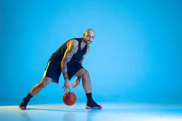 身体年轻的篮球队员穿着运动服训练 在运动中练习 运动在霓虹灯下隔离在蓝色的墙上运动的概念 运动 活力和活力 健康的生活方式射击篮球年轻