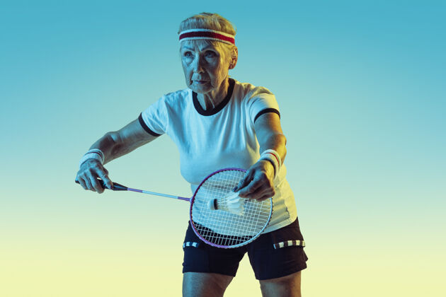 球拍在霓虹灯下穿着运动服在斜坡墙上打羽毛球的高级女士比赛球员健康