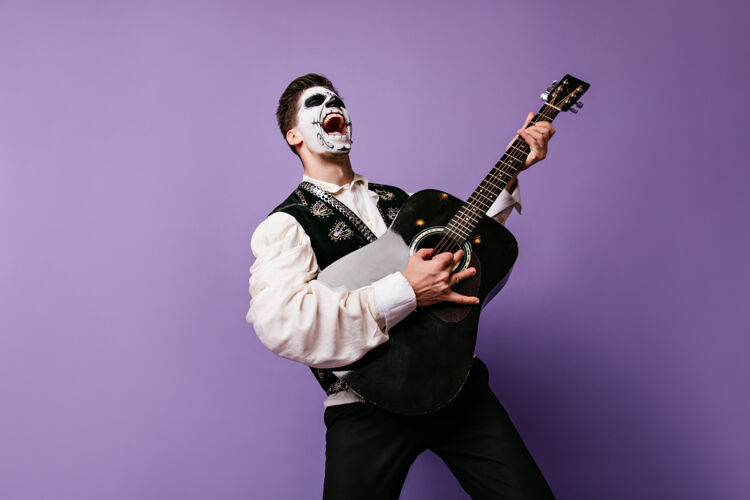 情感面部艺术的家伙想象自己的摇滚音乐家和情感姿态与吉他室内肖像的人在紫丁香墙上西班牙墨西哥幽灵