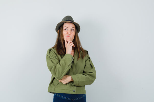 微笑年轻的女性穿着夹克 裤子 帽子站在思考的姿势 看上去犹豫不决正面图成人裤子年轻