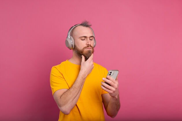 成人帅哥在随意地听着音乐 用耳机隔离在粉色背景上收音机耳机手