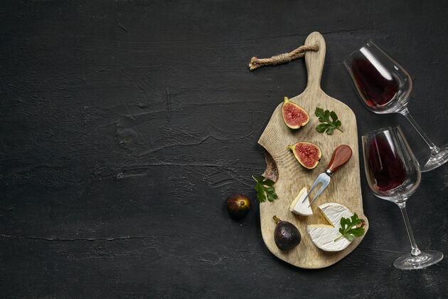 食物两杯红酒和一个美味的奶酪盘子 在黑石头上的木制厨房盘子上放着水果木材玻璃杯顶视图