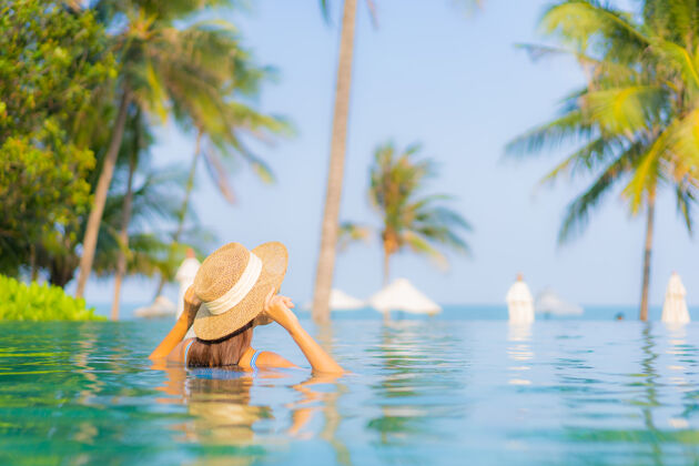 帽子肖像美丽的亚洲年轻女子放松微笑享受休闲围绕游泳池近海边度假海景享受健康女性