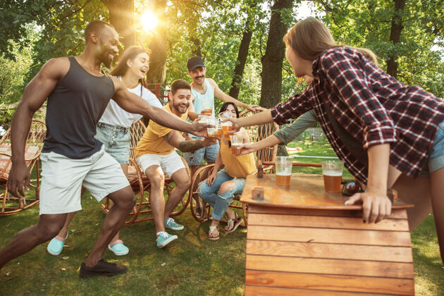 饮料一群快乐的朋友在阳光明媚的日子里喝着啤酒 一起烧烤一起在户外的林间空地或后院休息女人酒精品脱