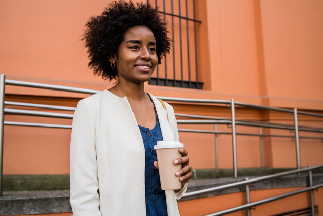 站立一张非洲裔女商人站在街上喝咖啡的照片商业和城市概念微笑办公室商务女性