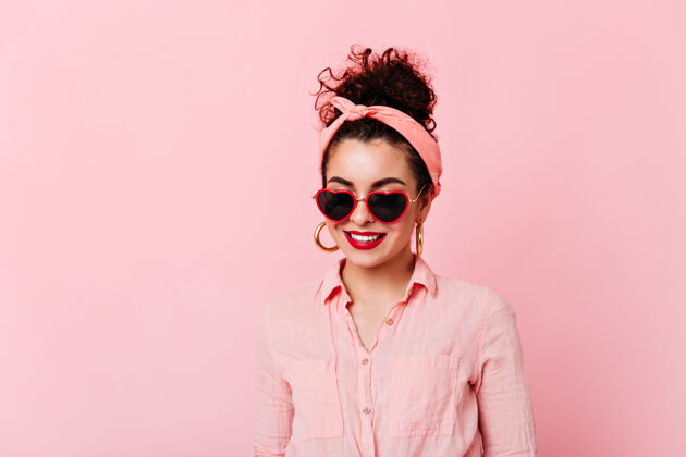 时尚戴着太阳镜的红唇发髻女孩的特写照片戴着粉色头带和棉质衬衫的女人在与世隔绝的空间里微笑复古衬衫情感