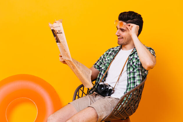 信心穿着格子衬衫和短裤的帅哥正坐在橙色的空间里 一边看报纸 一边休息太阳镜冒险潜水面具