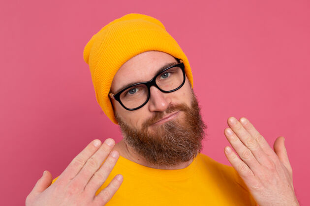 眼镜时尚帅气的留着胡子的欧洲男人的肖像 穿着休闲的黄色衬衫 戴着粉色背景的帽子和眼镜站帅哥欢呼