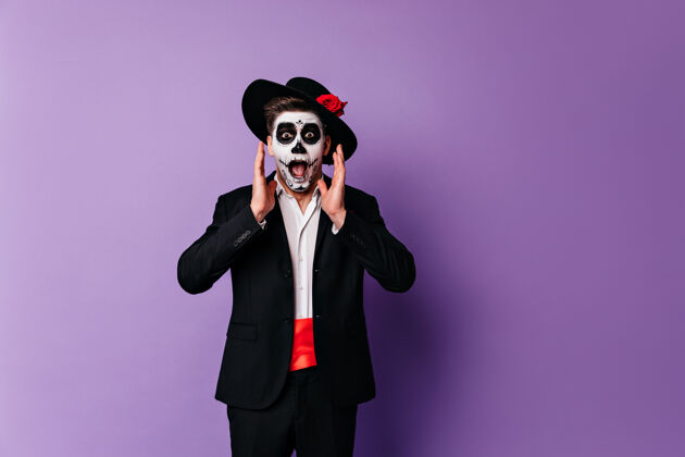 情感震惊的僵尸男子穿着优雅的衣服摆在紫色的背景在万圣节惊讶的家伙在墨西哥服装庆祝死亡日嘉年华恐怖惊人